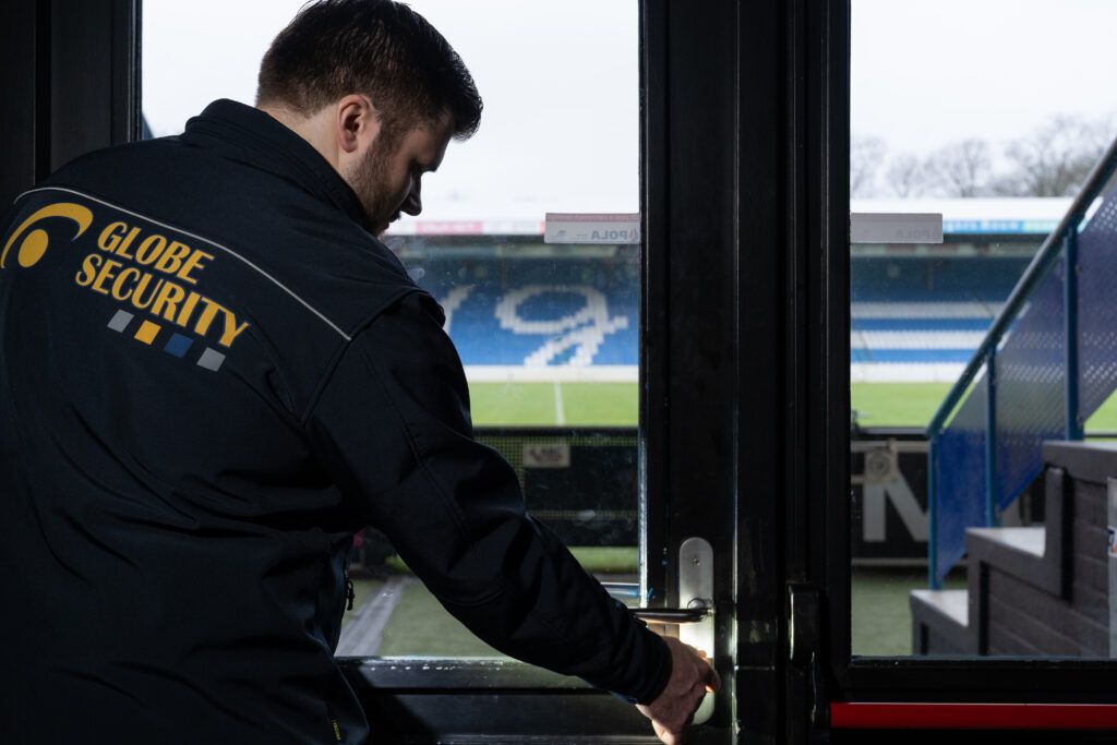 Beveiliger van Globe Security controleert een toegangsdeur in een voetbalstadion.