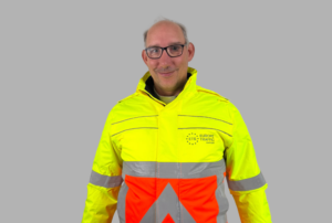 Medewerker van ETS Europe Traffic Support in geel-oranje veiligheidskleding met reflecterende strepen en bedrijfslogo.