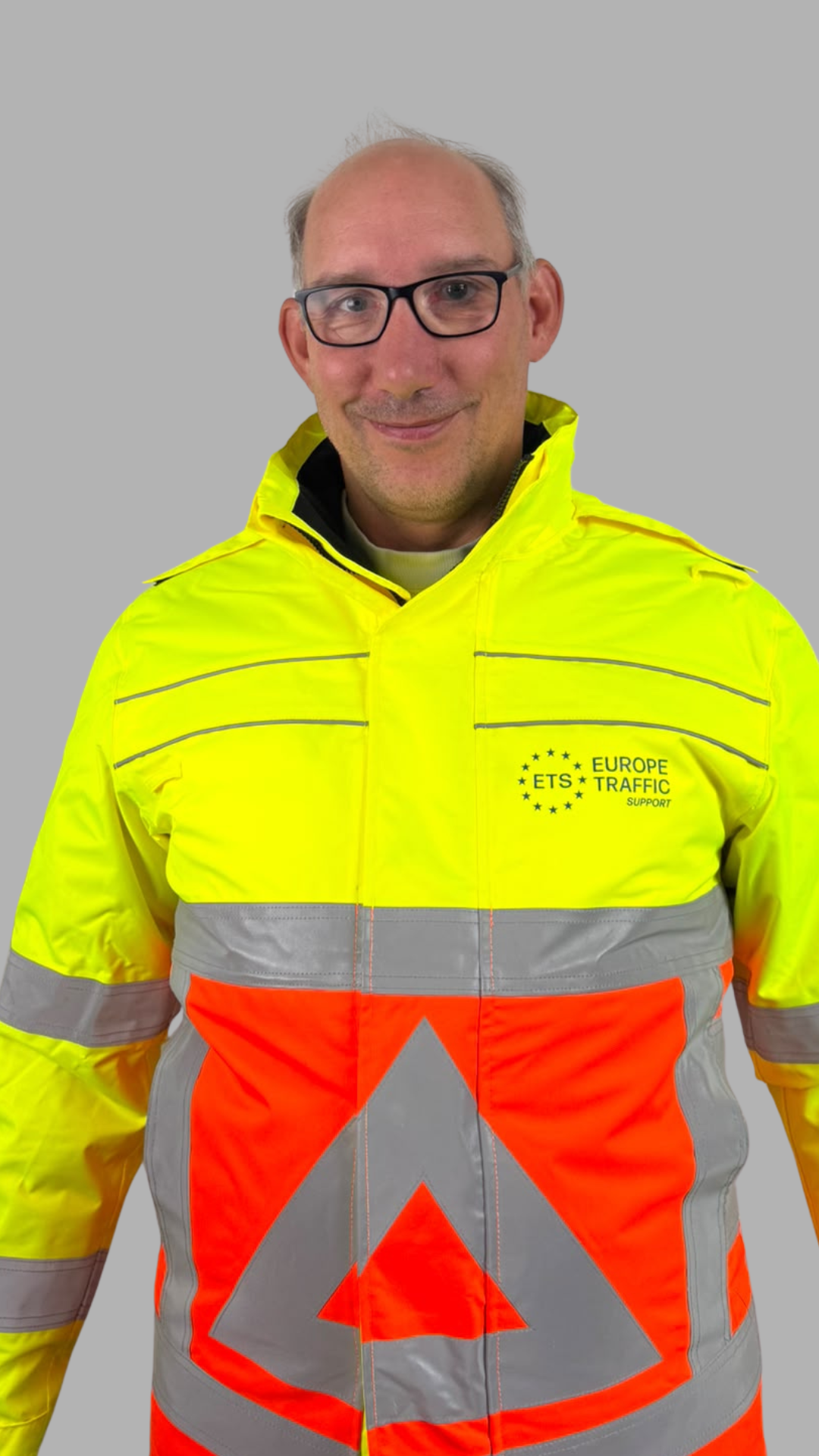 Medewerker van ETS Europe Traffic Support in geel-oranje veiligheidskleding met reflecterende strepen en bedrijfslogo.